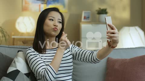 Young Woman In Striped Shirt Posing To The Smartphone Camera And Smiling While Taking A Selfie Photo