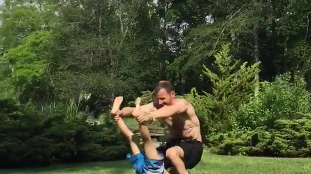 Father and son hold onto each other and roll on grass lawn