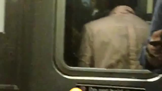 A man in a pink shirt dancing in between subway cars