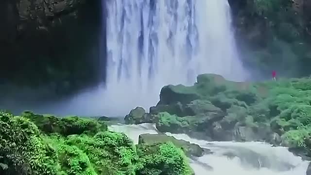 A waterfall cascades down the cliff from the hills behind.