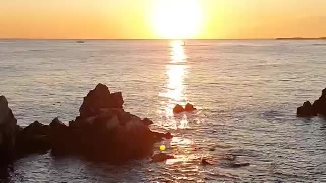 The hot sun. Bright sunrise. The sea and rocks.