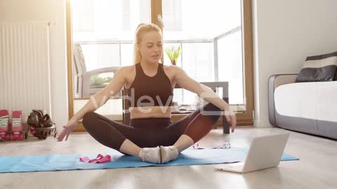 Beautiful sporty young woman in sportswear watching fitness video tutorials online on laptop