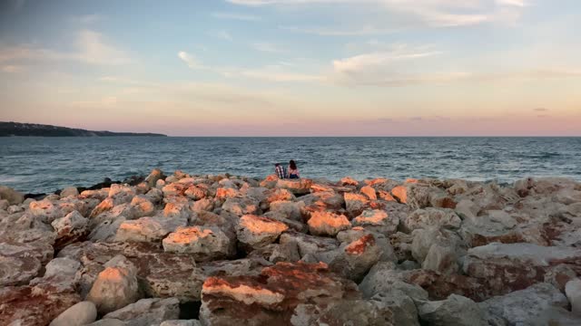 Couple sitting on rocks on the beach at sunset. A beautiful sunset.