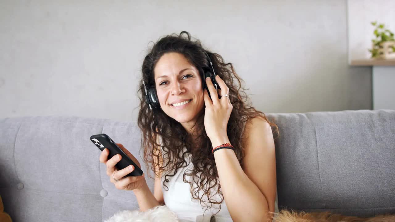 Relaxed woman with two pet dogs sitting indoors at home, listening to music