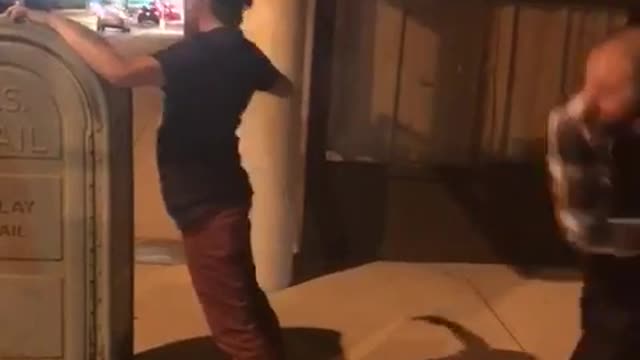 Guy in black shirt getting hit with belt on the street