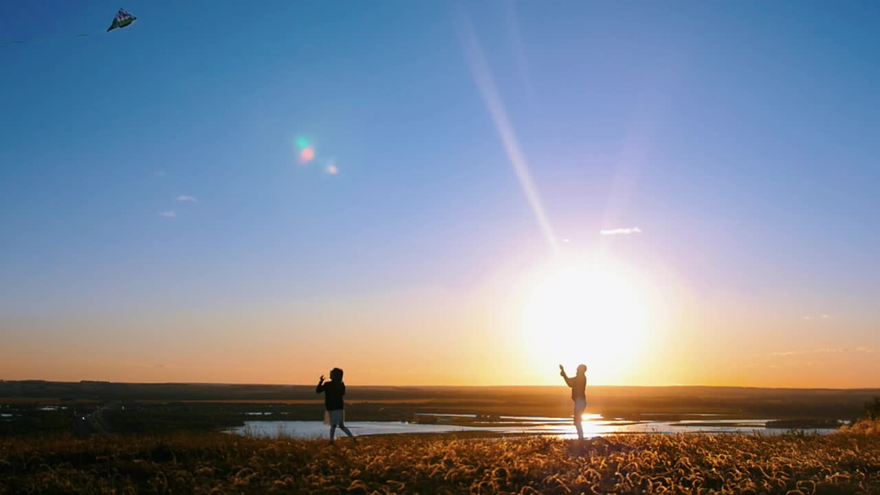 Man flying a kite and a girl running at sunset