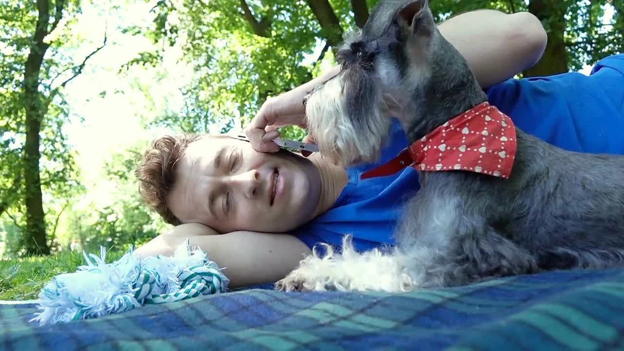 Happy boy chatting on cellphone while lying on the blanket with his cute dog