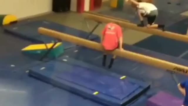 Red shirt kid hops on balance beam and falls backwards