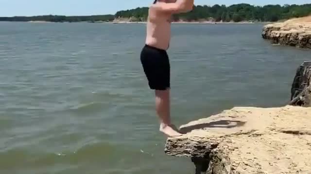 A man jumps off a cliff, which ends up cracking and he falls into the river