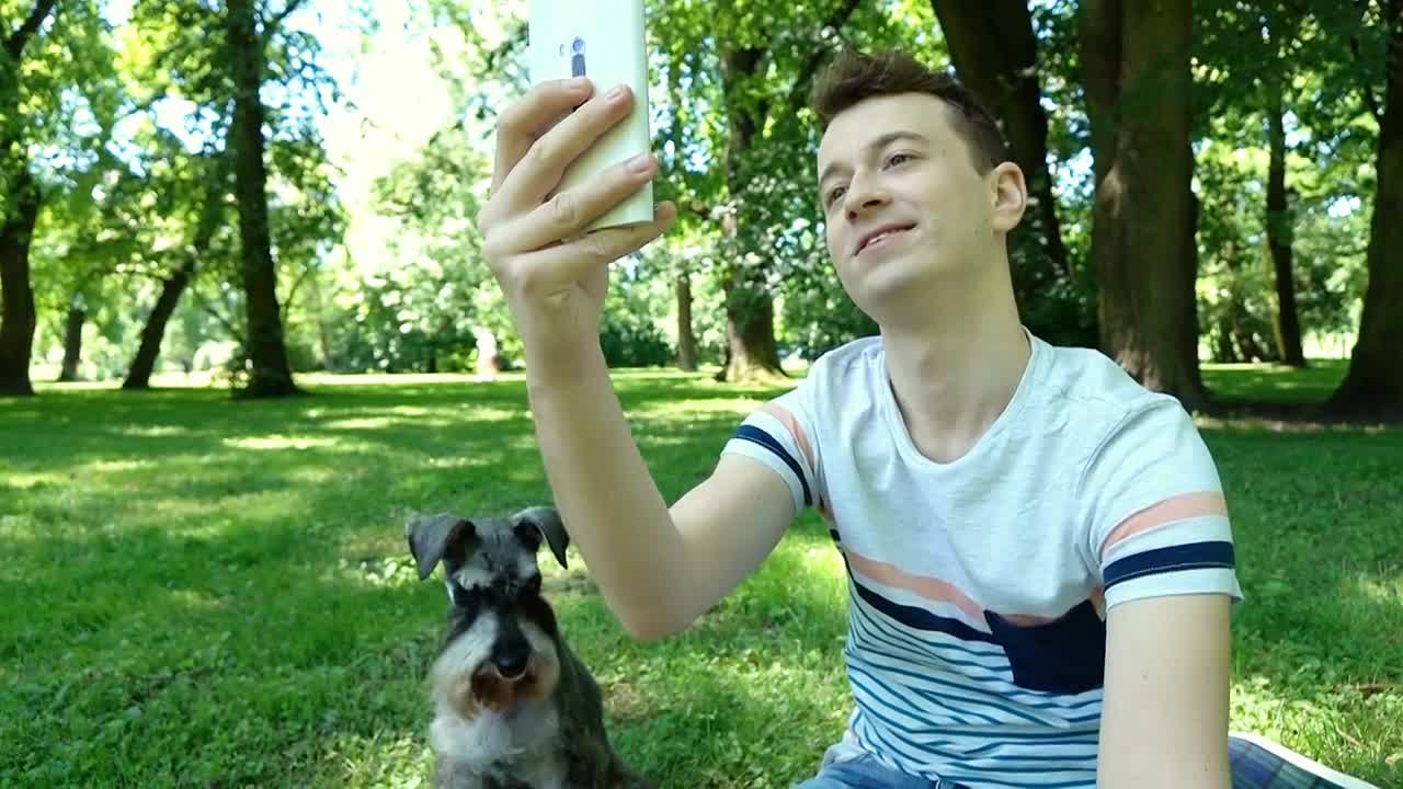 Boy having a videocall on smartphone while relaxing in the park with his dog