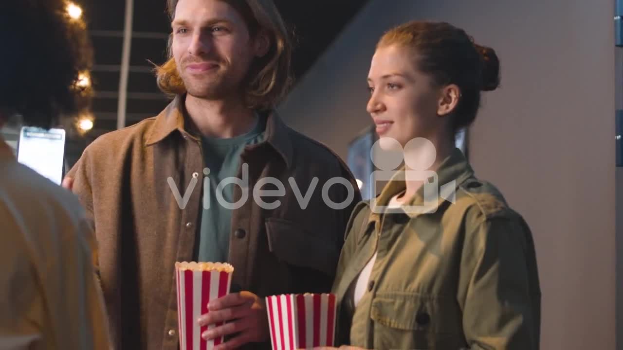 Happy Couple With Popcorn Box Showing Qr Movie Ticket On A Cell Phone At The Cinema