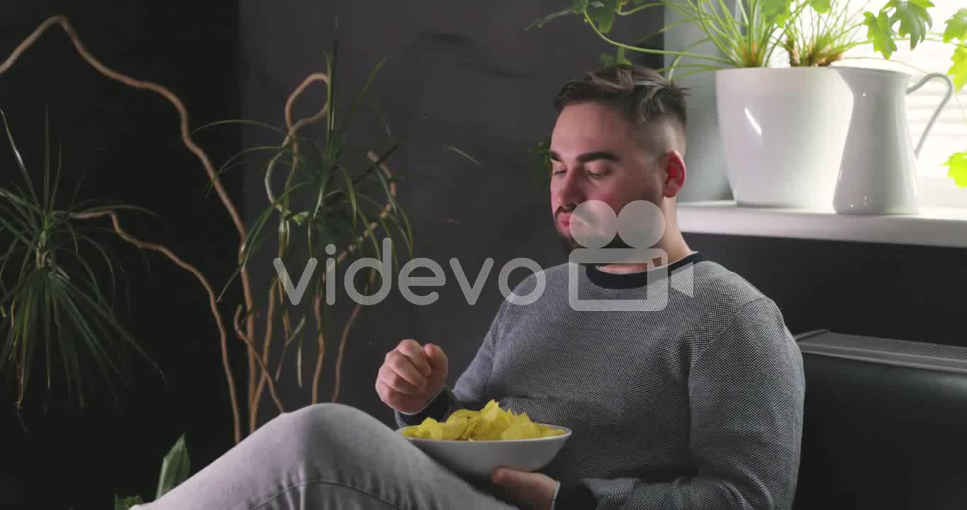 Hungry Man Sitting On Sofa And Eating Delicious Potato Chips