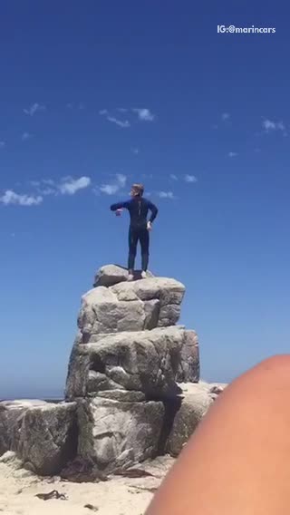 Kid dancing in wet suit on top of rocks at beach