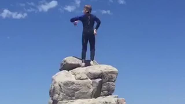 Kid dancing in wet suit on top of rocks at beach