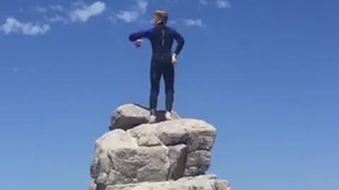 Kid dancing in wet suit on top of rocks at beach