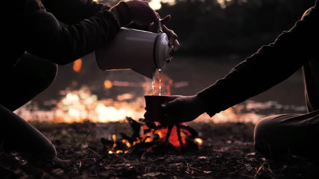 People pouring a warm drink around a campfire with Violet Spirit