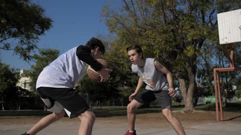 Two boys playing basketball at an outdoor court