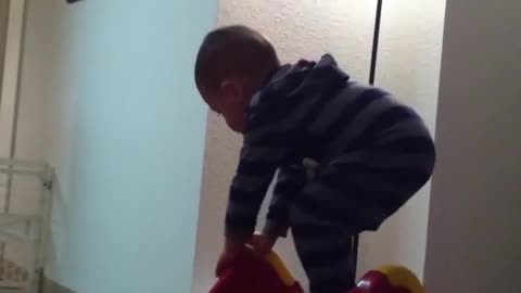 Little kid in striped sweater climbs up red slide and then falls the wrong way