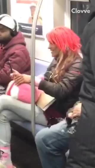 Woman in neon pink wig, pink socks, and brown crocs talks to herself on subway train