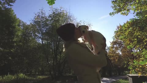 a woman is holding a puppy in a park in the sun