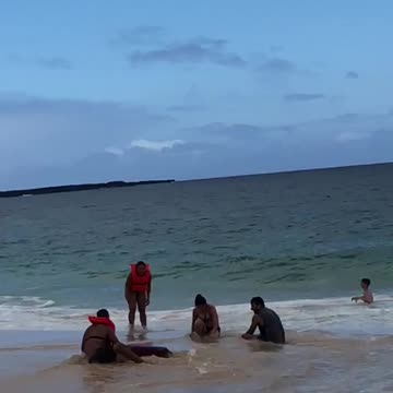 Three people tumble on the beach after wave throws them