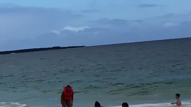 Three people tumble on the beach after wave throws them