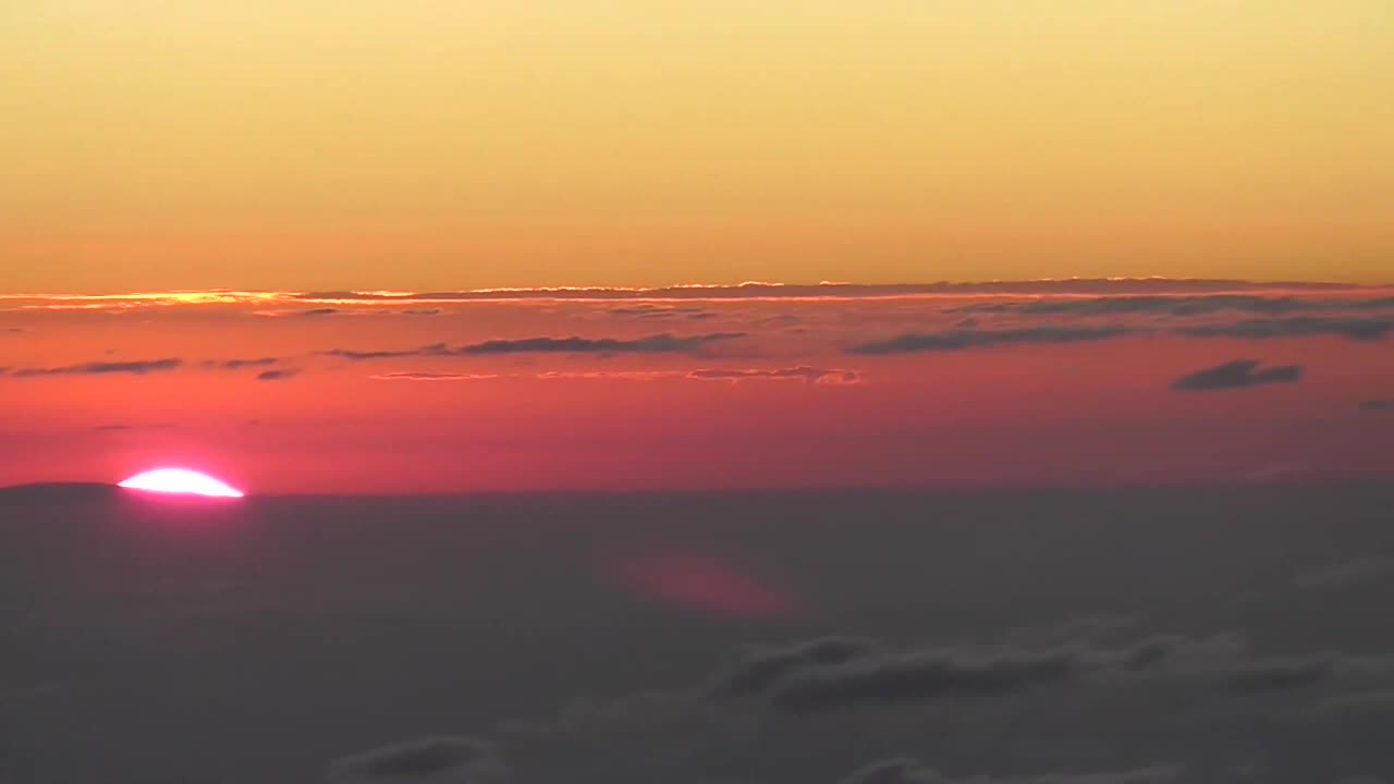 The sun rising out of the clouds in front of the horizon