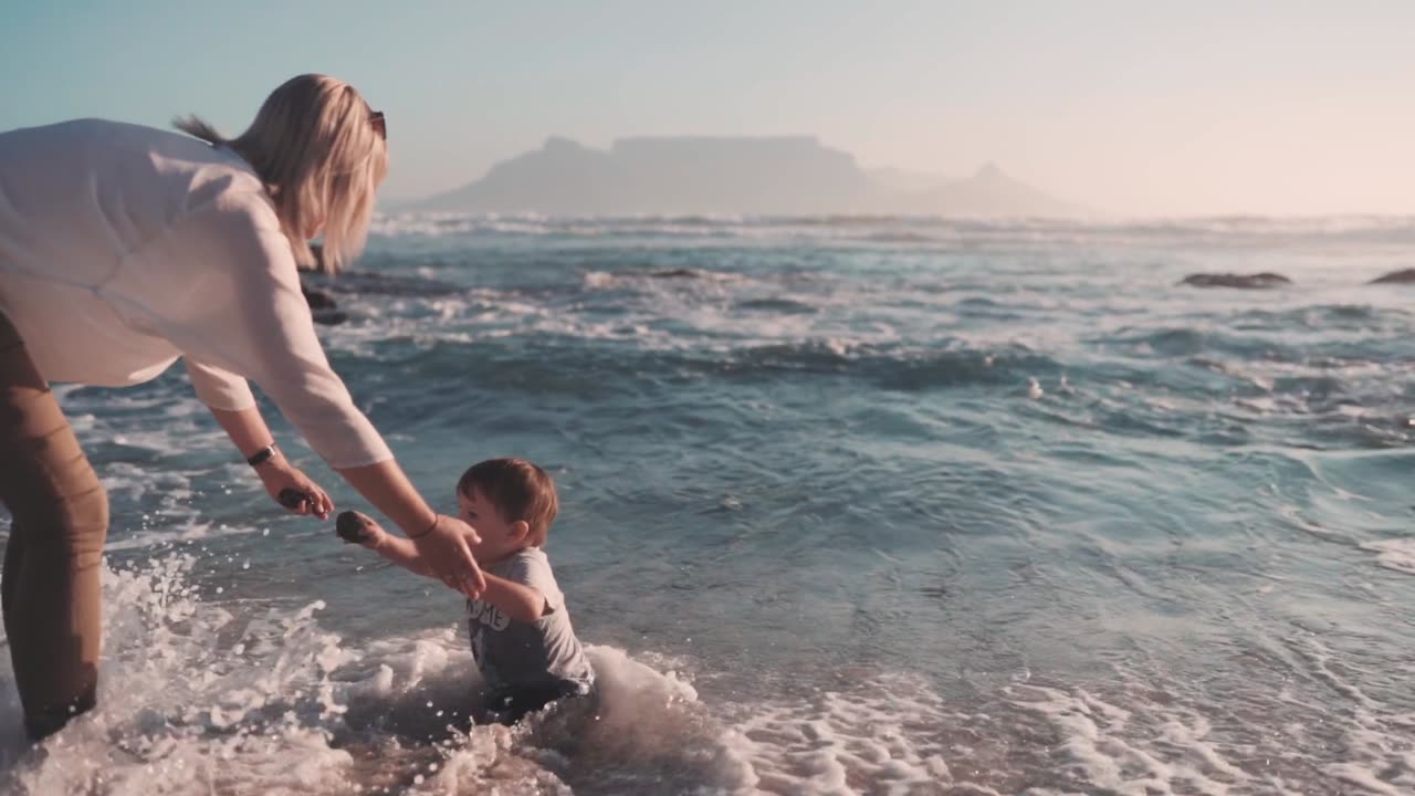 Mother Helping Her Child Get Up From A Stumble Cause By The Sea Waves