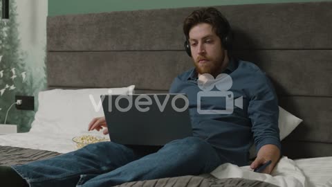 Boy Is Watching Videos On Laptop While Eating Popcorns On The Bed In Bedroom