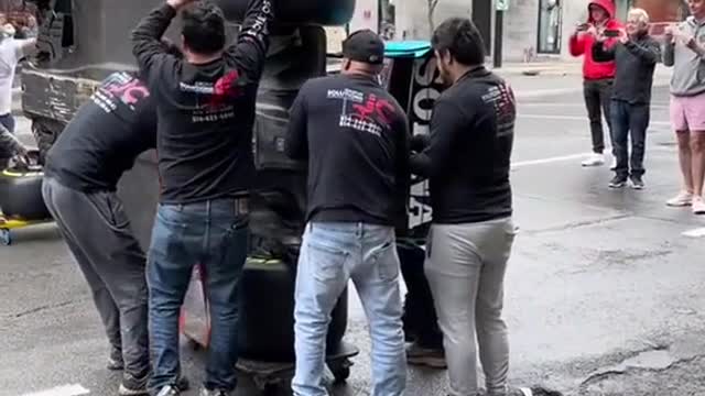 Many people work together to carry the racing car and get ready for the race.