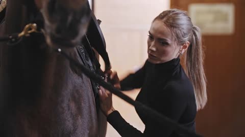 Woman putting on a saddle a horse on a leash