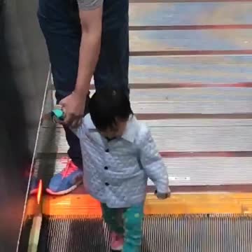 Little girl held by man walking on escalator