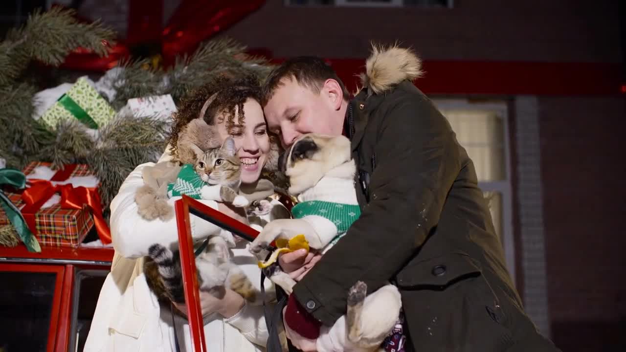 Happy couple holding pets on hands on Christmas evening decoration background outdoor