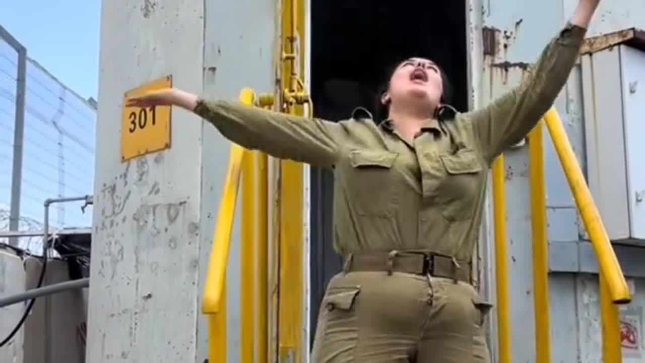 An Israeli female soldier stands in front of an Israeli tower