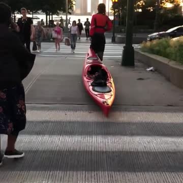 Guy in red dragging red kayak through metropolitan city streets