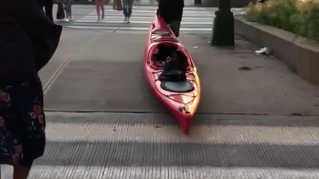 Guy in red dragging red kayak through metropolitan city streets