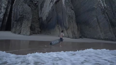 A man walking along a shore with his surfboard