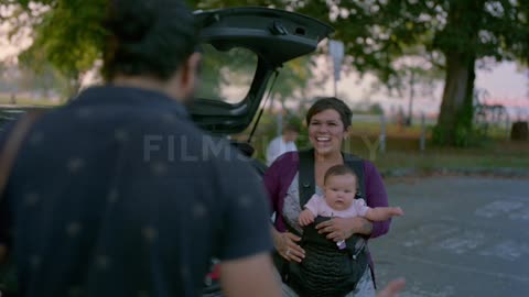 A man walks across a parking lot to greet a woman and her baby