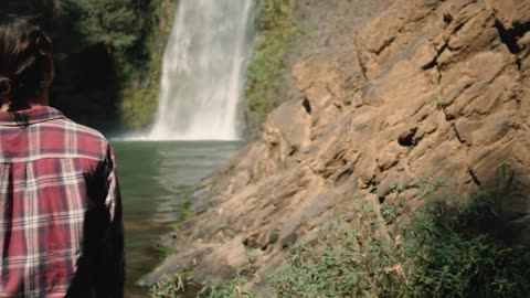 Woman standing in front of waterfall on a sunny day