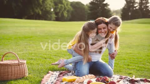 Two Cute Little Sisters Embracing Her Happy Mother From Back At Park During Picnic