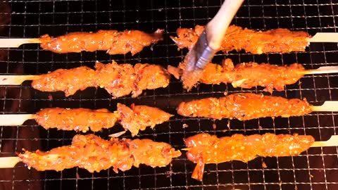 The skewers are brushed with dipping sauce and sizzled over the fire