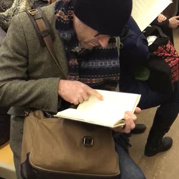 Old guy black beanie reading book pointing at words