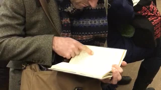 Old guy black beanie reading book pointing at words