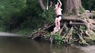 Shirtless man rope swing lands in shallow water