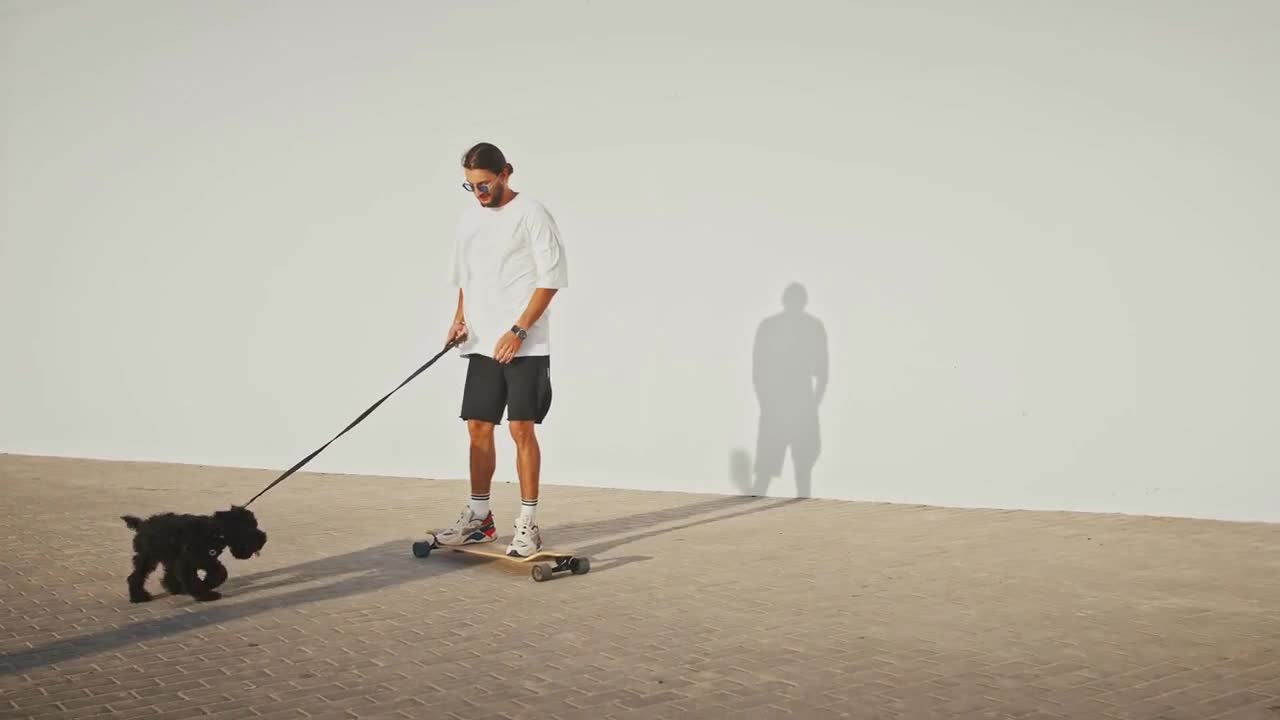 Young skater walking his dog, riding skateboard