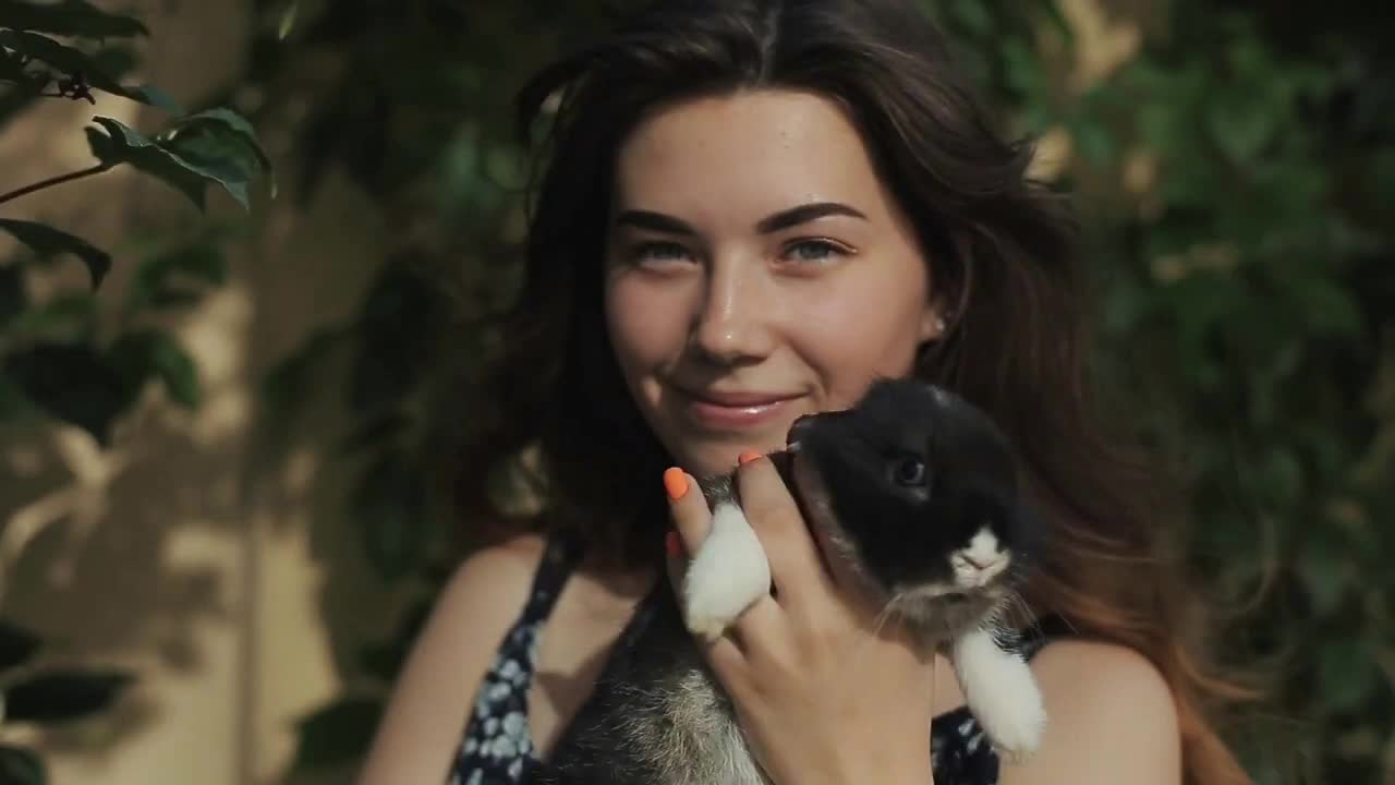 Young pretty woman stroking and kissing small fluffy rabbit in the garden in summer.