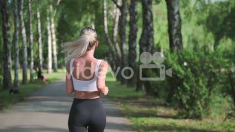 Back View Of A Pretty Blonde Girl Running In The Park