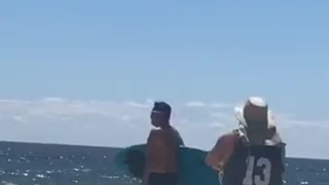 Guy with blue surfboard walking around on beach