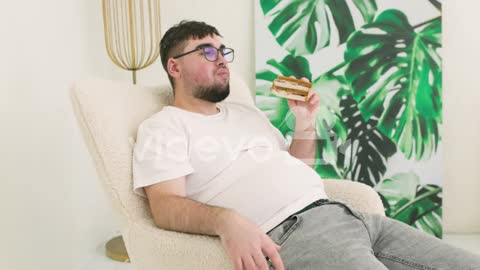Boy Touching His Belly Fat And Eating A Sandwich Sitting On Sofa