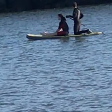 Guy in black wetsuit on surfboard with girl